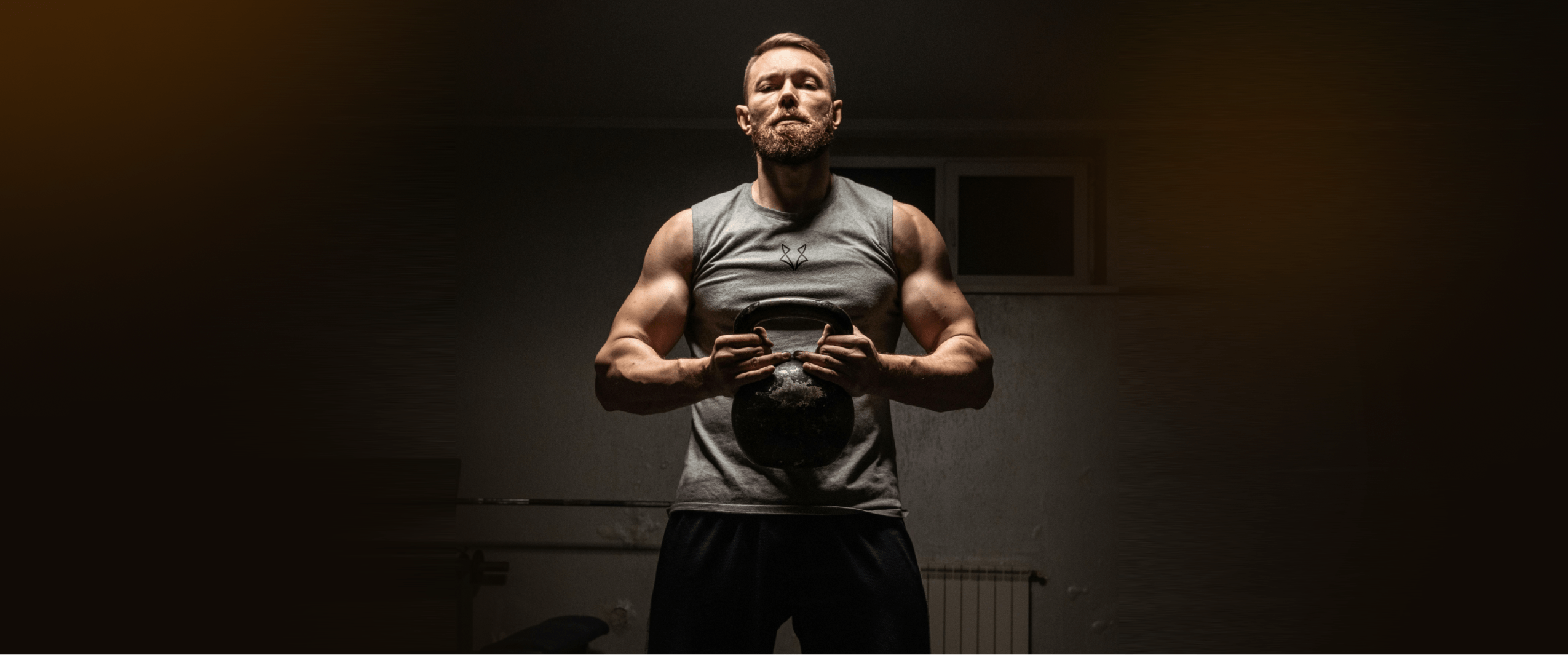 Muscular man lifting a kettlebell in a dimly lit gym, showcasing strength and focus during a workout.